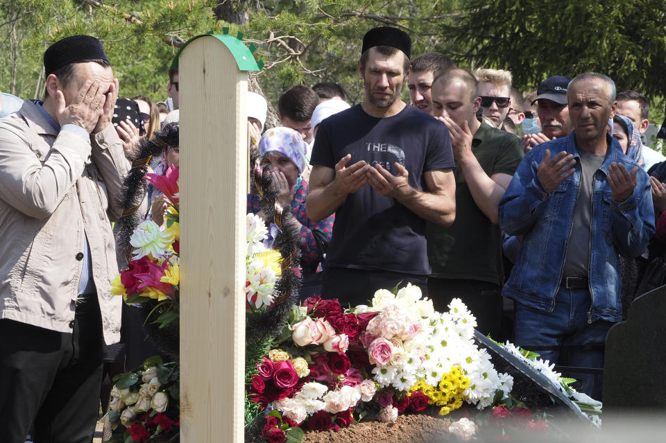 People pray next to the grave of Elvira Ignatieva, an English language teacher who was killed at a school shooting on Tuesday in Kazan, Russia, Wednesday, May 12, 2021. Russian officials say a gunman attacked a school in the city of Kazan and Russian officials say several people have been killed. Officials said the dead in Tuesday's shooting include students, a teacher and a school worker. Authorities also say over 20 others have been hospitalised with wounds. (AP Photo/Dmitri Lovetsky)