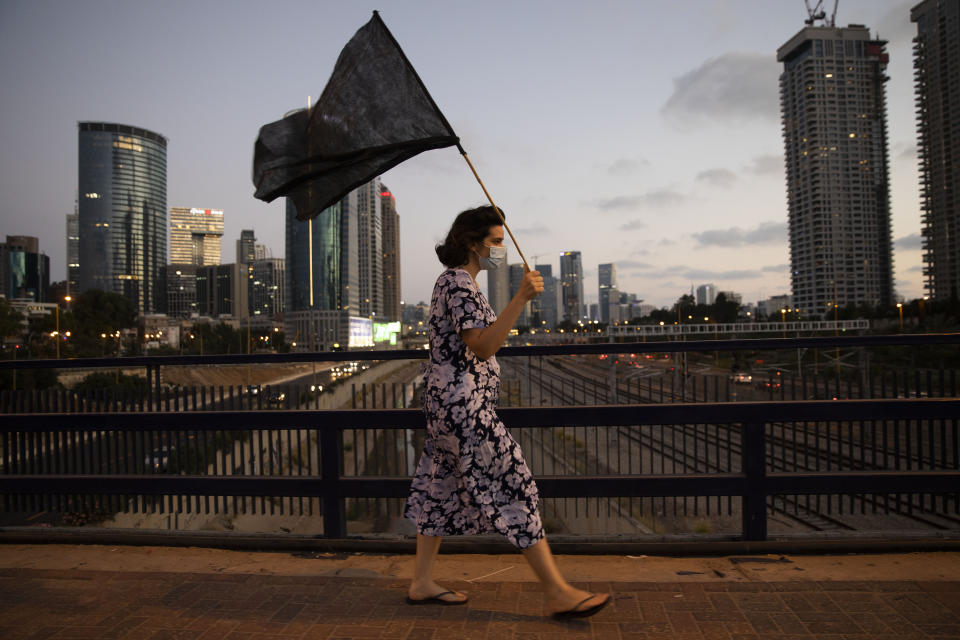 A woman wears a protective face mask, to protect against coronavirus, walks with a black flag during a protest against Israeli Prime Minister Benjamin Netanyahu, in Tel Aviv, Israel, Saturday, July 18, 2020. (AP Photo/Oded Balilty)