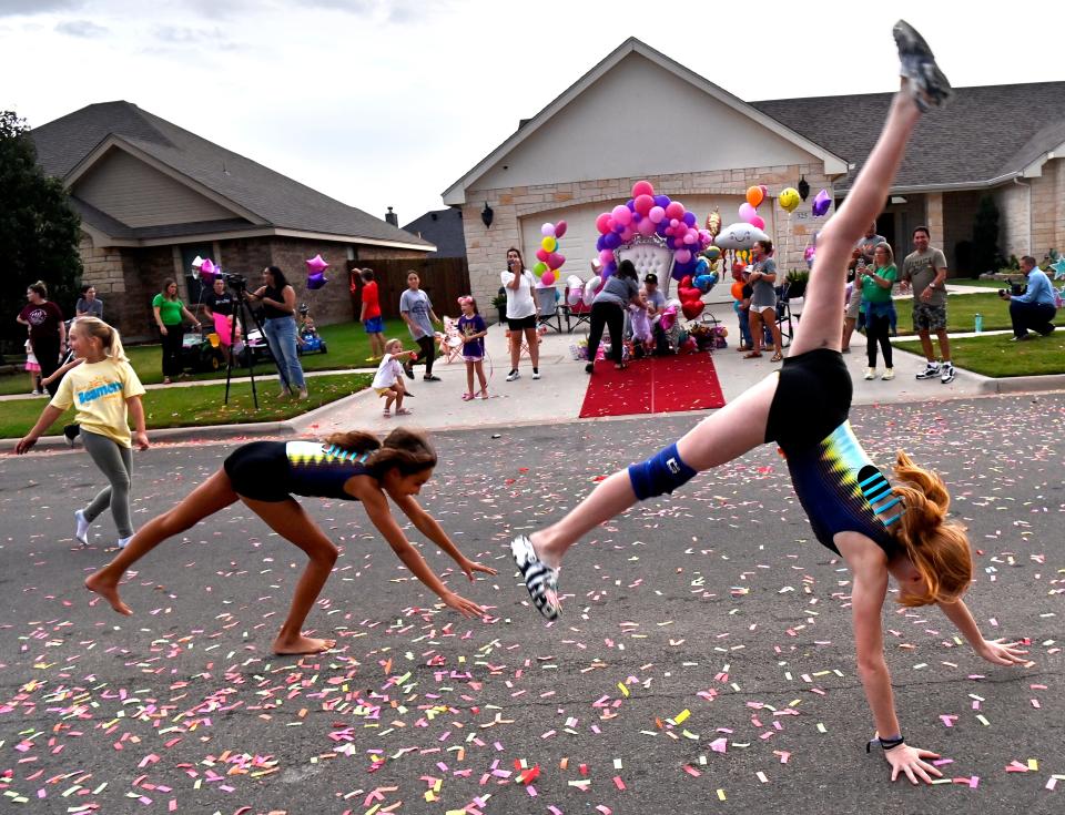 Gymnasts perform cartwheels and flips for Sienna Molina seated with her father Tony on a throne in the background in the family driveway.