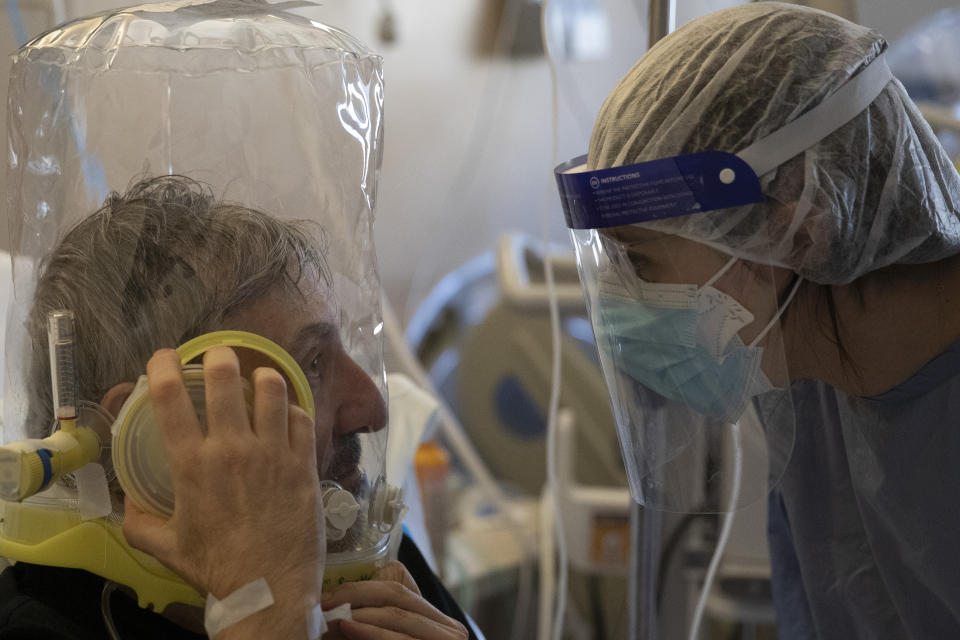 60-year-old Nazzareno Santilli, breathing under oxygen CPAP (continuous positive air pressure) headgear ventilation, talks to Dr. Elisabetta Teti in the sub-intensive COVID-19 unit of the Tor Vergata Polyclinic Hospital, in Rome, Saturday, Nov. 7, 2020. Communication is challenging when patients wear oxygen helmets and Teti is covered by layers of protective gear. (AP Photo/Alessandra Tarantino)