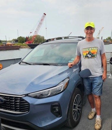 Mark Taylor of Clarkston stands beside his 2024 Ford Escape Hybrid while taking a ferry in northern Michigan on Sept. 11, 2024.