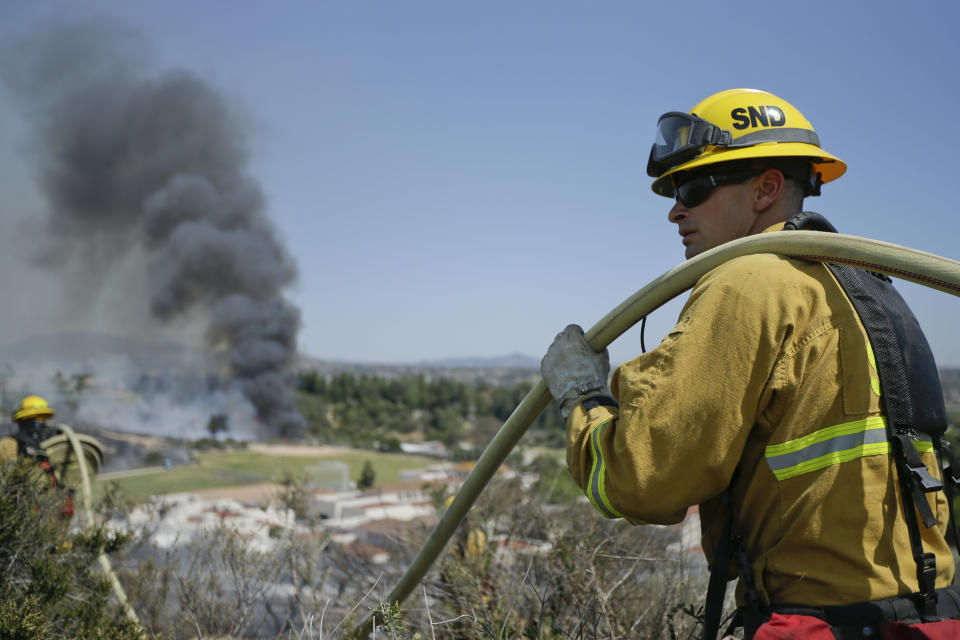 A firefighter carries hose during a wildfire Wednesday, May 14, 2014, in Carlsbad, Calif. A fast-moving wildfire ignited hillsides and destroyed more than two dozen homes Wednesday in the coastal city of Carlsbad as weary firefighters scrambled to control multiple blazes in Southern California on the second day of a sweltering heat wave. (AP Photo)