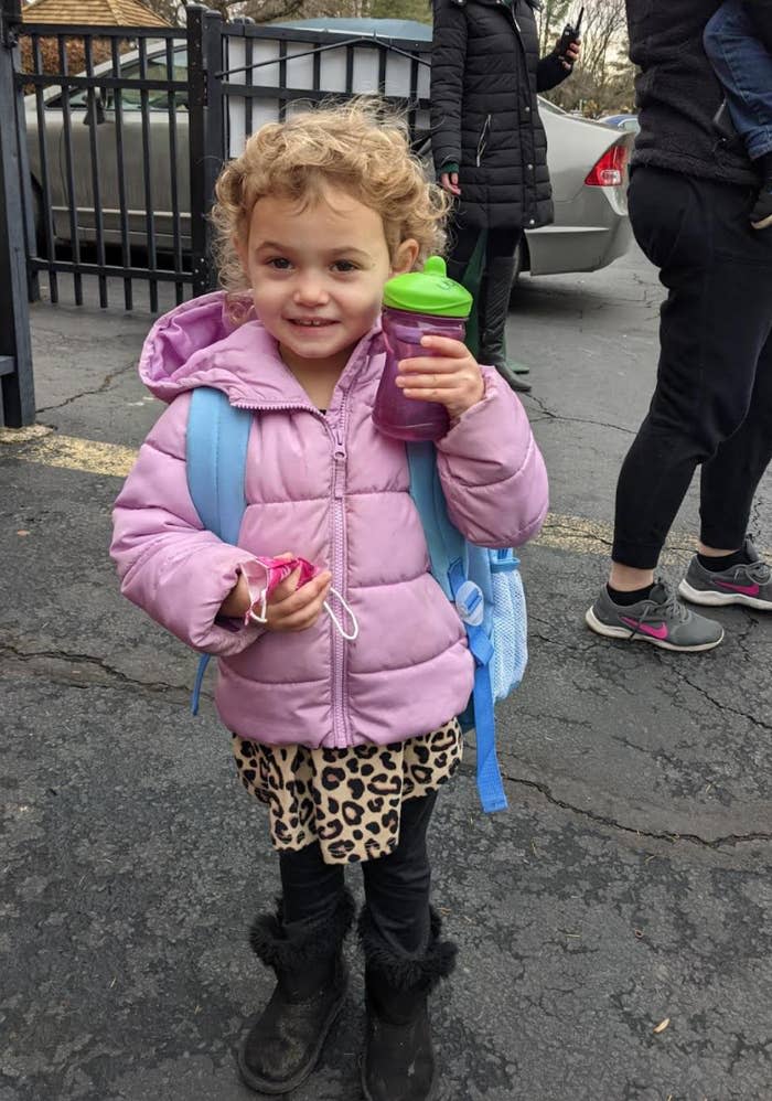 Peyton with her backpack on holding up her sippy cup and smiling