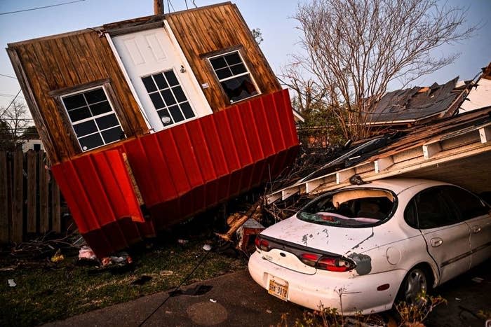 A small building completely turned upside down next to a car that is under rubble