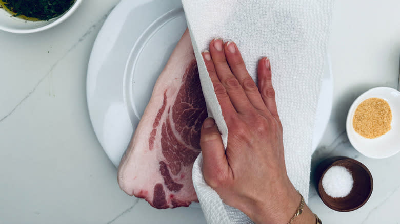 hand wiping pork steak with paper towel