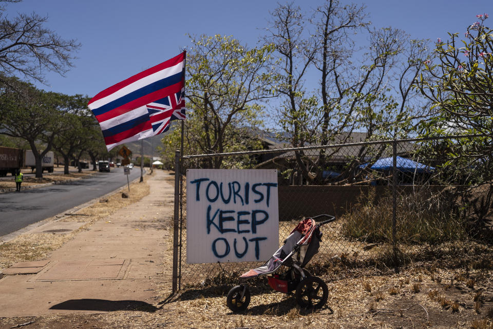 A sign that says "Tourist Keep Out" is seen next to a Hawaiian flag hanging upside down in Lahaina, Hawaii, Thursday, Aug. 17, 2023. The blazes incinerated the historic island community of Lahaina and killed more than 100 people. (AP Photo/Jae C. Hong)