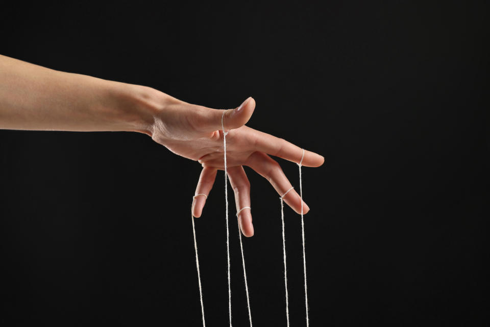 A woman's hand pulling the strings of a puppet.