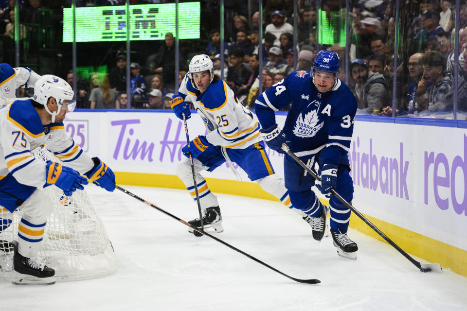 Toronto Maple Leafs center Auston Matthews (34) moves the puck around the net while defended by Buffalo Sabres defenseman Owen Power (25) and defenseman Connor Clifton (75) during the second period of an NHL hockey game Saturday, Nov. 4, 2023, in Toronto. (Christopher Katsarov/The Canadian Press via AP)