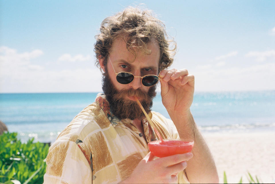 Man on a beach drink a cocktail with a straw