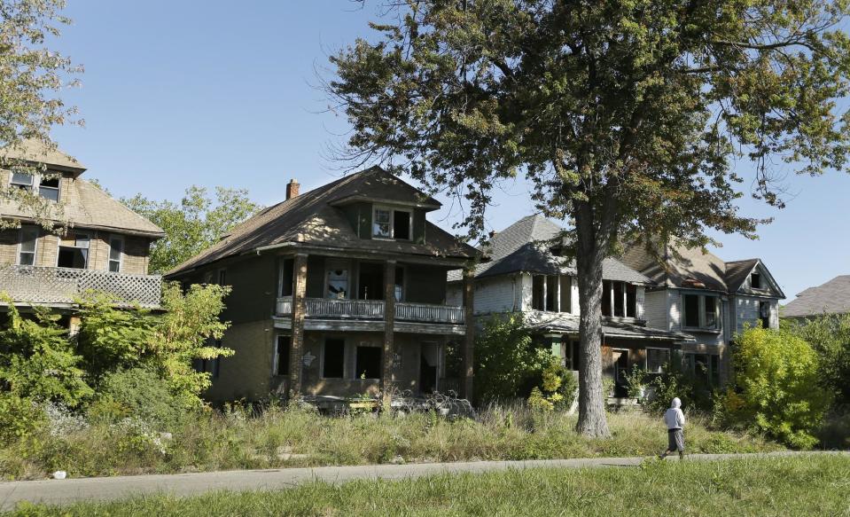 FILE - In this Sept. 26, 2013 file photo a young man walks in front of a row of abandoned houses in Detroit. Detroit has thousands of decrepit and abandoned homes and buildings. The city’s proposal to emerge from bankruptcy includes a plan to demolish them. (AP Photo/Carlos Osorio, File)