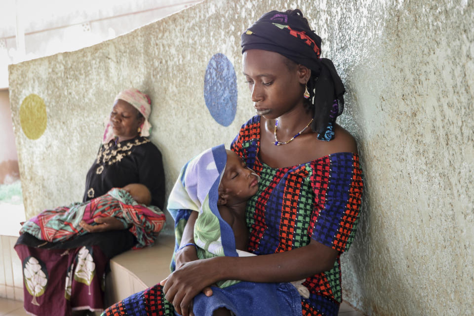 Fatima Li, de 20 años, en primer plano, sostiene a su hijo Hama Sow de 2 años que está conectado a una sonda de alimentación porque padece desnutrición, y Hadiara Ouedraogo, a la izquierda, carga a su nieta Fatimata Ouedrago, de 2 años, que padece edema debido a desnutrición avanzada, el lunes 22 de junio de 2020 en la Universidad Yalgado Ouedraogo, en Uagadugú, Burkina Faso. (AP Foto/Sam Mednick)