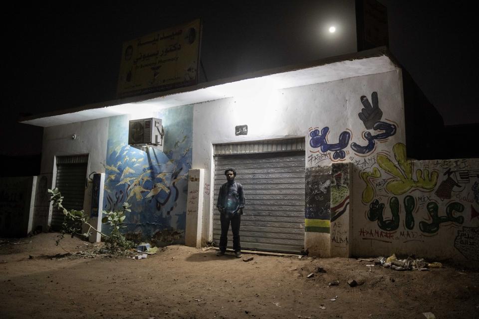 This Jan. 12, 2020 photo shows, Sudanese activist and artist Youssef al-Sewahly stands near graffiti he drew during last years' revolution, on a street in Khartoum, Sudan. When al-Sewahly took to the streets in Sudan late in 2018, he and the other protesters had one goal: to remove the autocratic regime of Omar al-Bashir and replace it with a civilian-led government. They’ve achieved the former, but the latter still hangs in the balance. (AP Photo/Nariman El-Mofty)