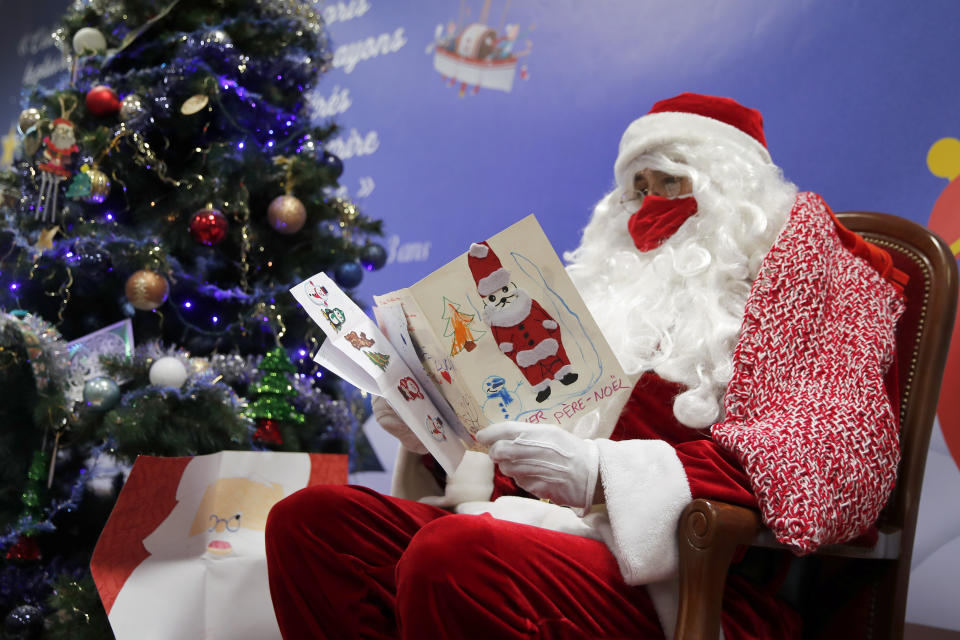 A postal worker dressed as Santa, reads letters to addressed to "Pere Noel" - Father Christmas in French - decorated with love hearts, stickers and glitter, in Libourne, southwest France, Monday, Nov. 23, 2020. Letters pouring by the tens of thousands into Santa's mailbox offer a glimpse into the worries and hopes of children awaiting a pandemic-hit Christmas. Along with usual pleas for toys and gadgets, kids are also mailing requests for vaccines, for visits from grandparents, for life to return to the way it was. The office estimates that one letter in three mentions the pandemic. (AP Photo/Francois Mori)