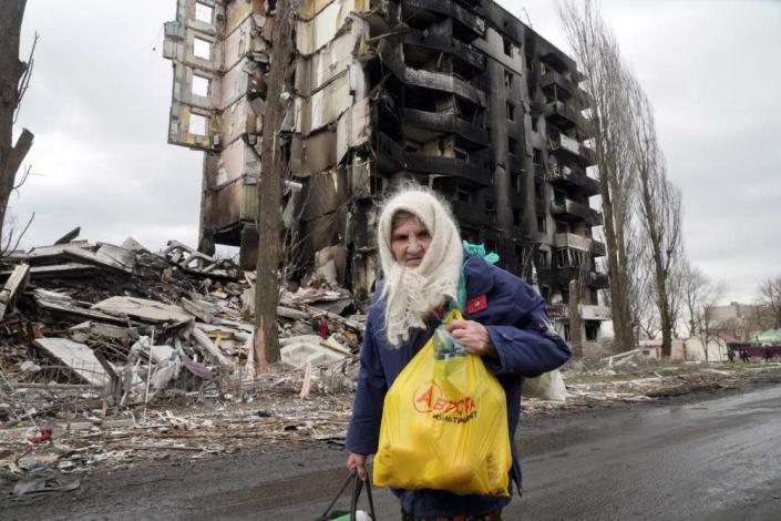 An elderly woman walks by an apartment building destroyed in the Russian shelling in Borodyanka, Ukraine, Wednesday, April 6, 2022.