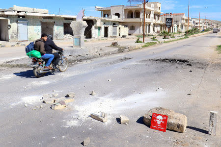 Men ride a motorbike past a hazard sign at a site hit by an airstrike on Tuesday in the town of Khan Sheikhoun in rebel-held Idlib, Syria April 5, 2017. The hazard sign reads, "Danger, unexploded ammunition". REUTERS/Ammar Abdullah
