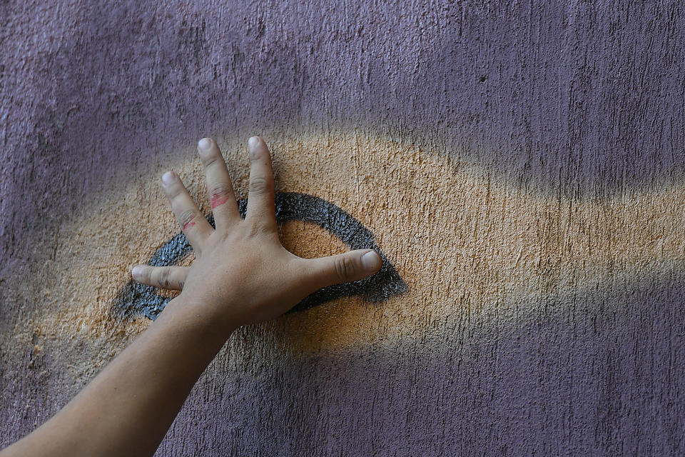 Street artist Wolfgang Salazar uses his hand to measure proportions as he begins to paint the eyes of his most recent mural, in the Boleita neighborhood of Caracas, Venezuela, Monday, Dec. 28, 2020. Salazar says he's part of a campaign to legitimize the street art of graffiti and has been invited to several countries in Latin America and Europe to paint murals. (AP Photo/Matias Delacroix)