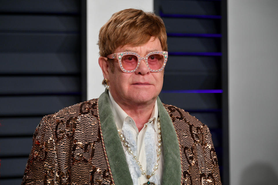 Elton John on a red carpet wearing a bedazzled blazer and pink glasses. (Getty Images)