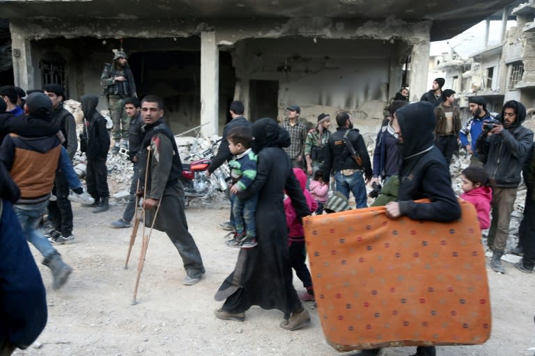 Syrians walk down a destroyed street as they prepare to evacuate one of the few remaining rebel-held pockets in Eastern Ghouta, on the outskirts of the Syrian capital Damascus, on March 24, 2018