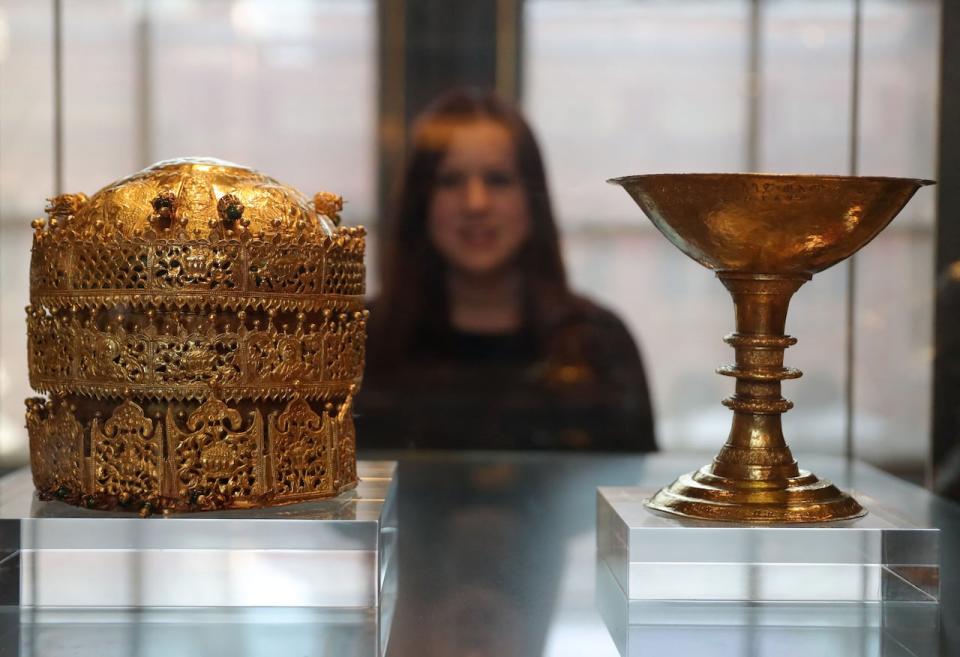 A employee poses in front of a Crown (L), made in Ethiopia around 1740, made of gold and gilded copper with glass beads, pigment and fabric and a gold chalise, made by Walda Giyorgis in Gondar, Ethiopia between 1735 and 1740 at an exhibition, "Maqdala 1868, A reflection on the 1868 siege and battle at Maqdala", at the Victoria and Albert Museum in central London, on April 5, 2018. 