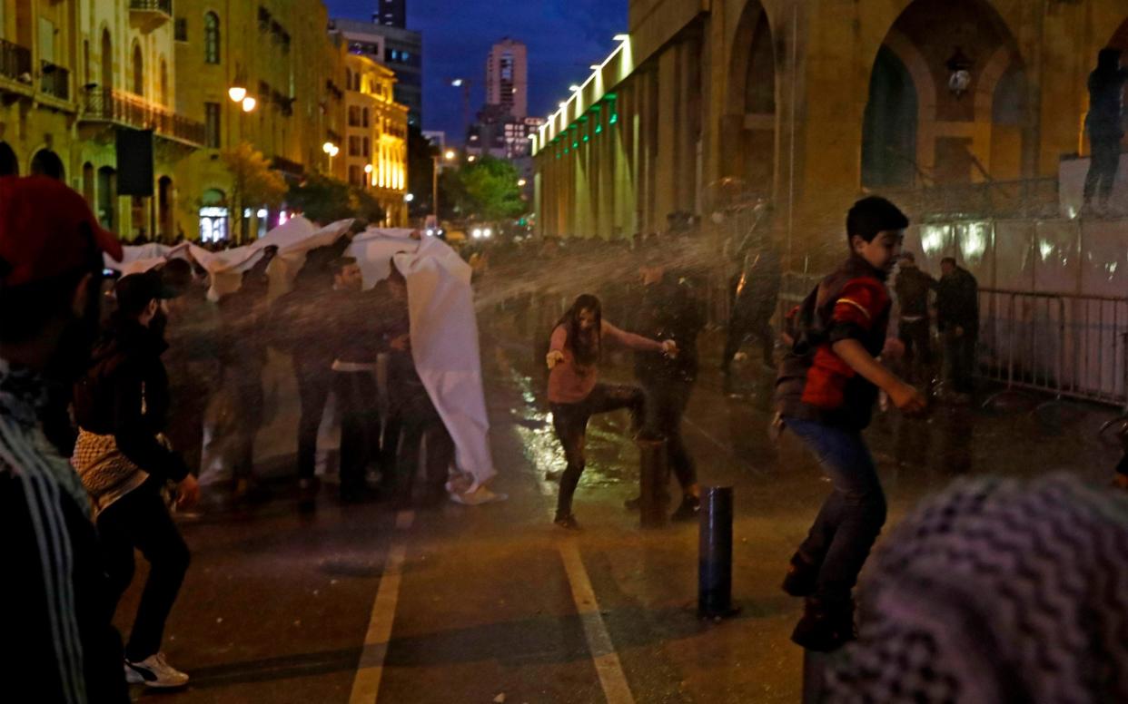 Lebanese anti-government protesters use a banner as shelter from water jets during clashes with security forces near Parliament in Beirut - AFP