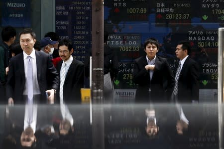 FILE PHOTO: People walk in front of board displaying stock indexes in Tokyo