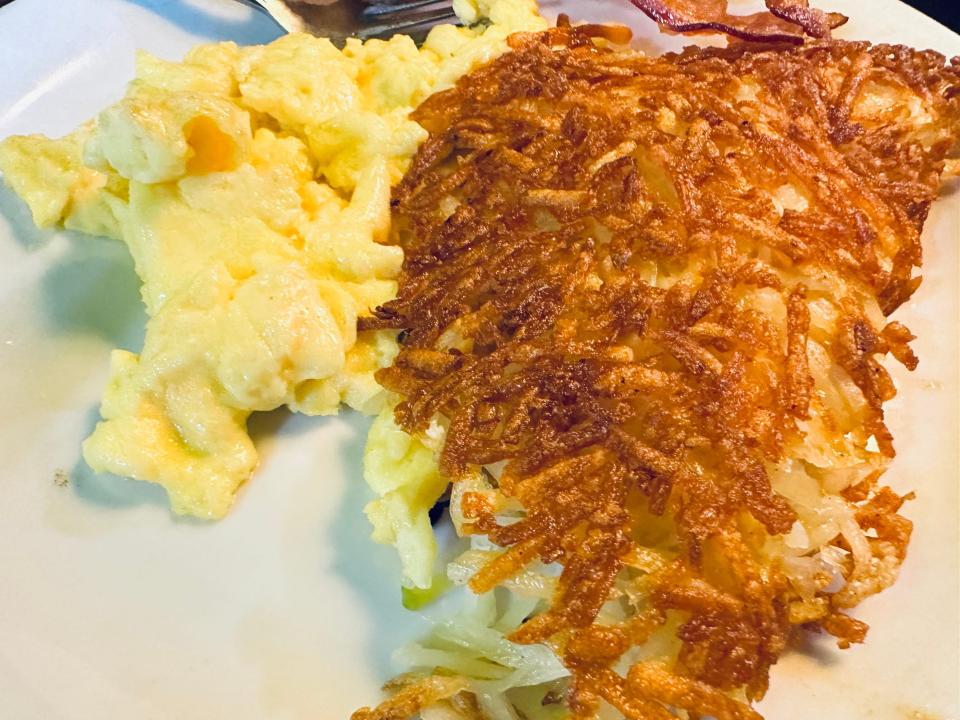 Denny's crispy hash browns on white plate along with eggs and bacon