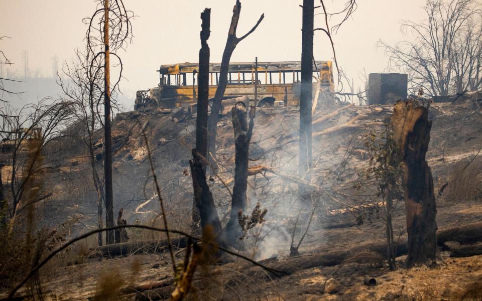 A burnt out school bus sit on a hill after the Bear Fire - Shutterstock