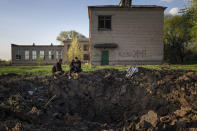 FILE - People look at a crater created by a Russian rocket attack in a schoolyard in Dobropillya, Donetsk region, eastern Ukraine, Thursday, April 28, 2022. Despite the widespread damage and destruction to educational infrastructure, war crimes experts say proving an attacking military’s intent for individual schools is difficult. (AP Photo/Evgeniy Maloletka, File)