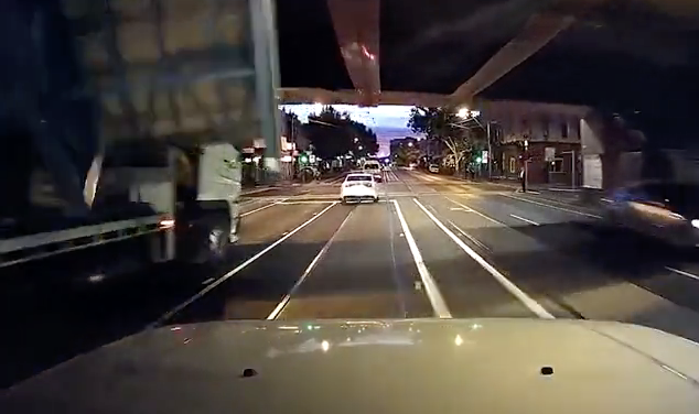 Dashcam image from a truck driving into an overpass and spilling its load onto a small car.