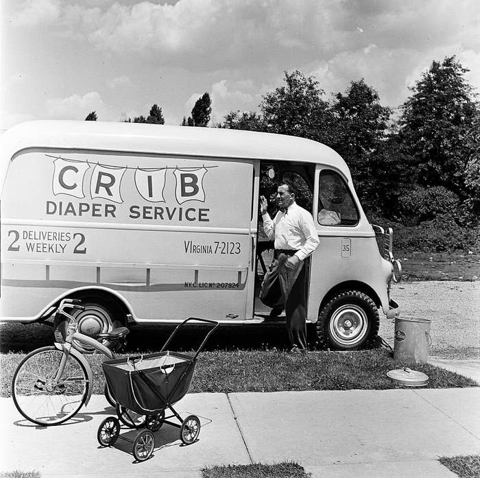 A man stands beside a van labeled "CRIB Diaper Service" holding a phone. A baby carriage and tricycle are in the foreground