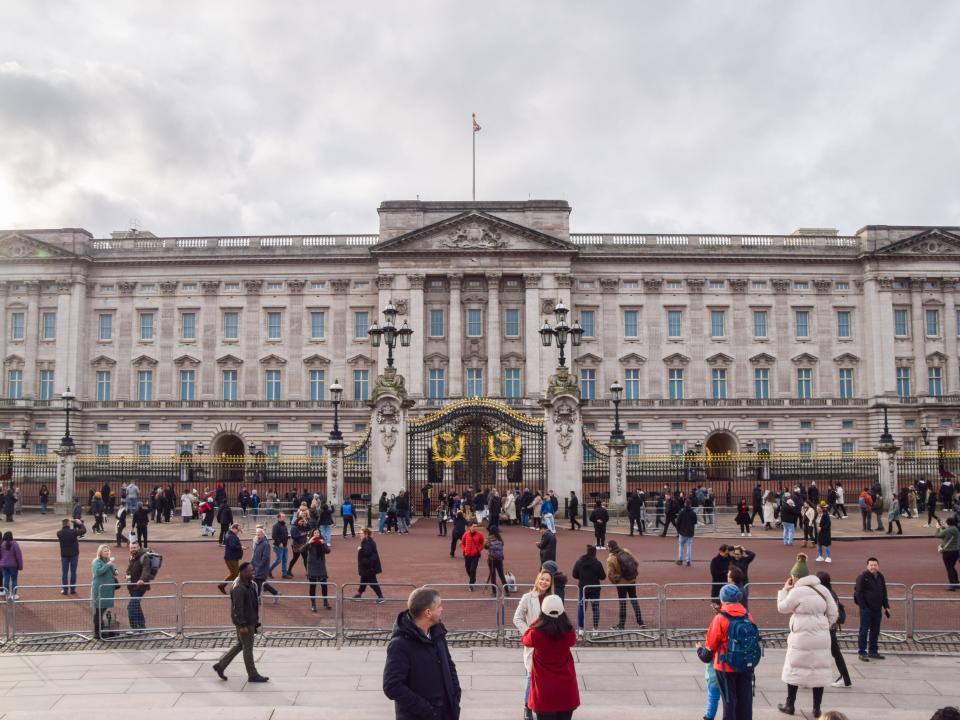 A crowd of people stands in front of Buckingham Palace.