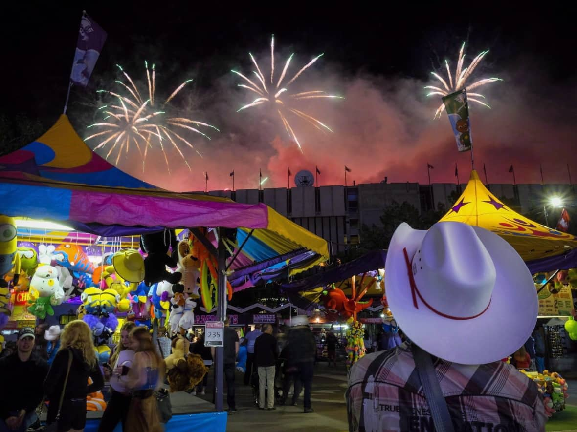 A visitor watches the fireworks display from the midway at the Calgary Stampede in 2016. The annual festival takes over much of the city, complete with pancake breakfasts, beer-soaked barbecues and corporate boxes at rodeo events. (Jeff McIntosh/The Canadian Press - image credit)