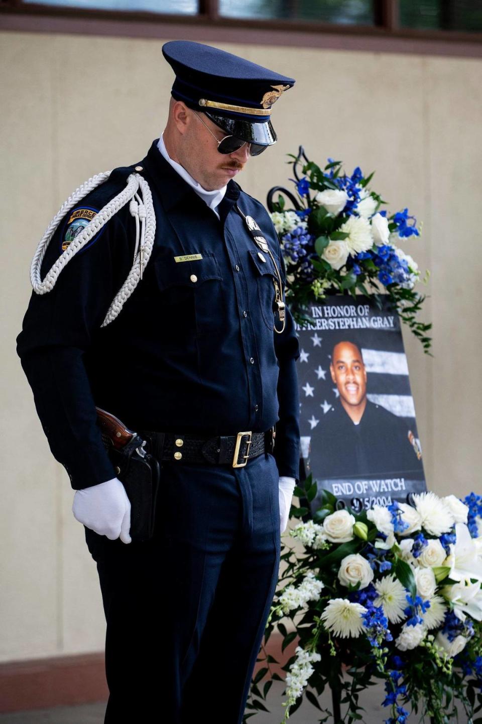 A Merced police officers stands near a photo of fallen Merced police officer Stephan Gray as a moment of silence is observed during an annual ceremony to honor Gray at the Merced Police Station in Merced, Calif., on Monday, April 15, 2024. Gray was shot and killed in the line of duty on April 15, 2004.