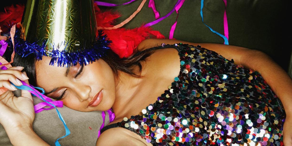 young woman wearing sequin dress and party hat sleeping on sofa