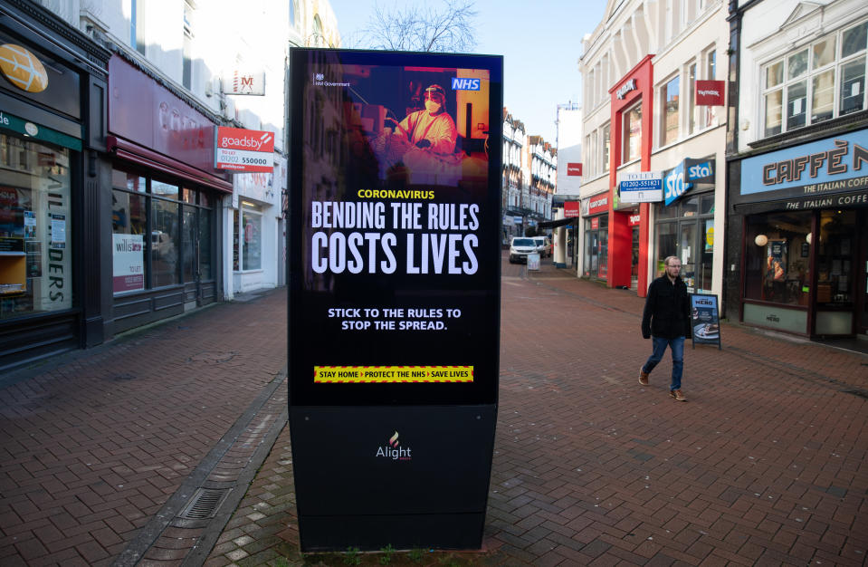 A person passes a 'Bending the rules costs lives' government coronavirus sign on Old Christchurch road in Bournemouth, during England's third national lockdown to curb the spread of coronavirus. Picture date: Friday January 22, 2021.