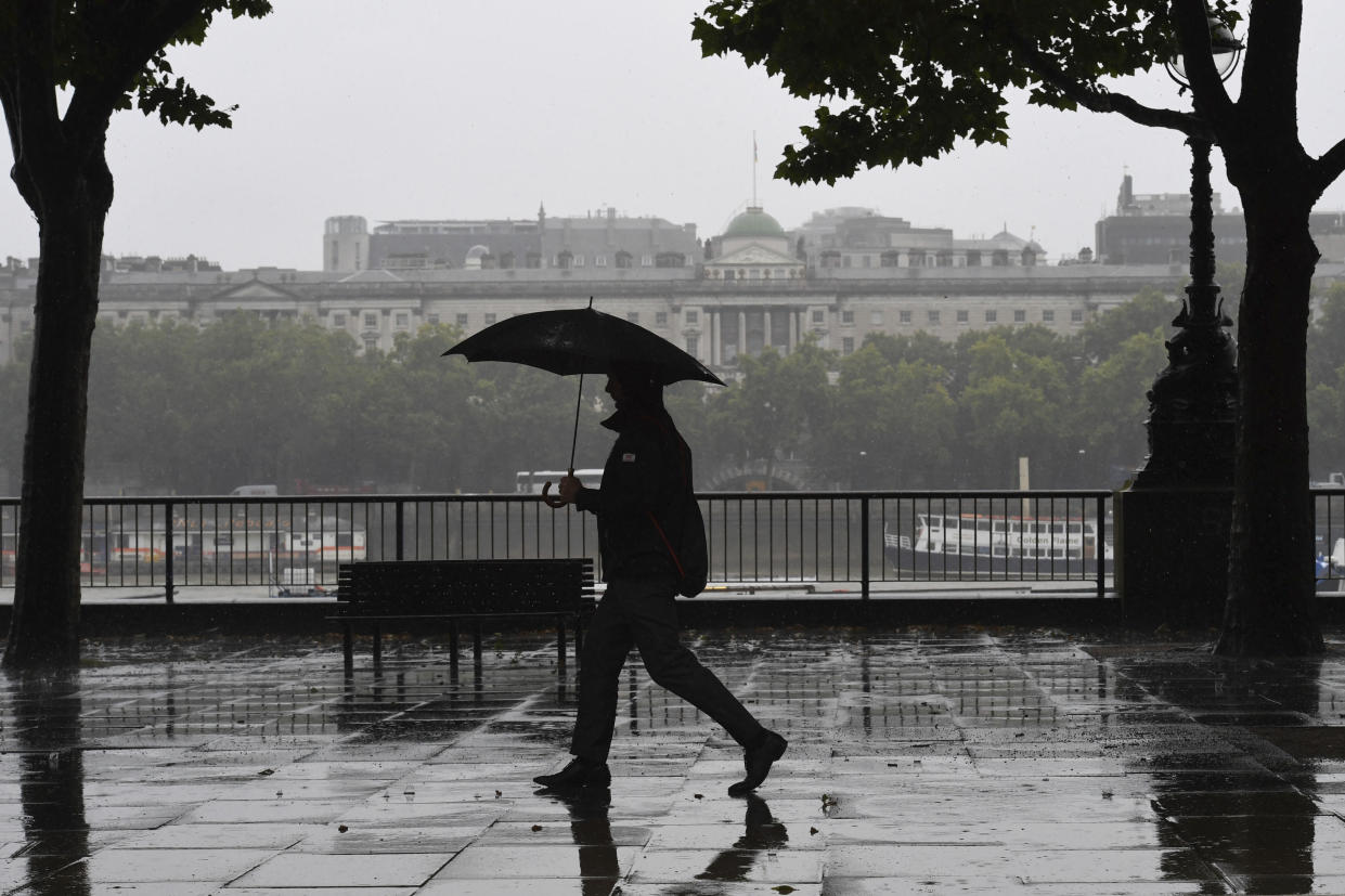 A man walks in the rain along the River Thames Embankment footpath in central London, Friday July 19, 2019.  After a period of hot sunny weather, much of Britain is suffering under rain clouds and a cold front.(Stefan Rousseau/PA via AP)