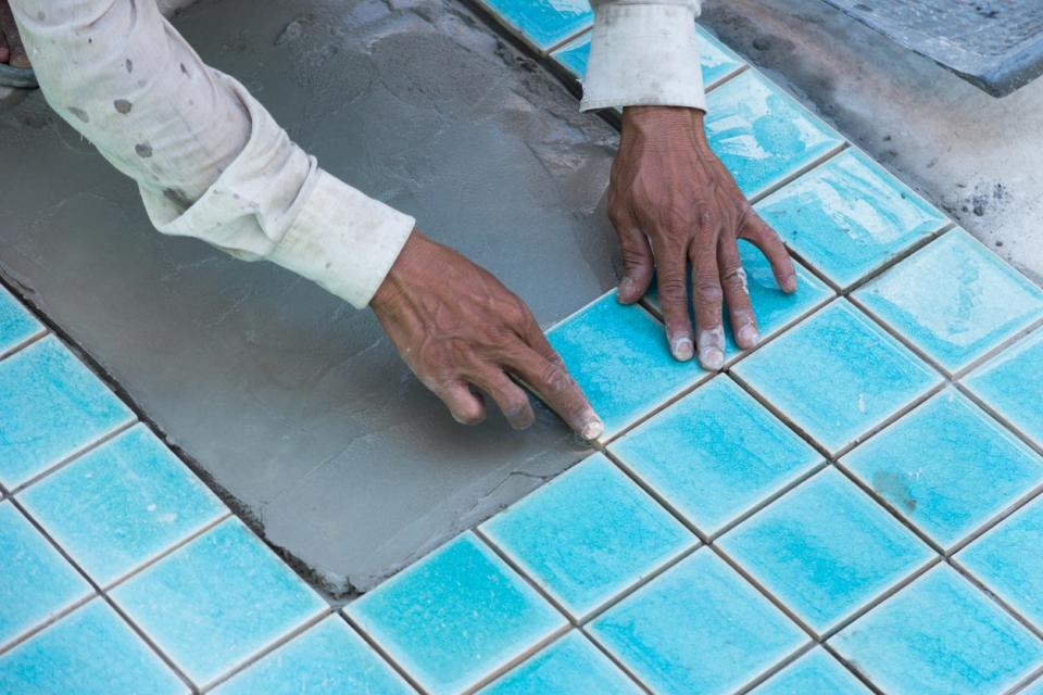 A close up of a worker's hands laying down blue tile for a pool.