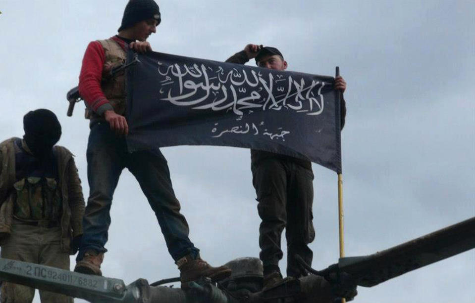 FILE - In this Friday, Jan. 11, 2013 file citizen journalism image provided by Edlib News Network, ENN, which has been authenticated based on its contents and other AP reporting, rebels from al-Qaida affiliated Jabhat al-Nusra waving their brigade flag as they step on the top of a Syrian air force helicopter, at Taftanaz air base that was captured by the rebels, in Idlib province, northern Syria. Syria’s uprising was not destined to be quick. Instead, the largely peaceful protest movement that spread across the nation slowly turned into an armed insurgency and eventually a full-blown civil war. More than 130,000 people have been killed, and more than 2 million more have fled the country. Nearly three years after the crisis began, Syria's government and opposition are set to meet in Geneva this week for the first direct talks aimed at ending the conflict. The Arabic words on the flag reads, "There is no God only God and Mohamad his prophet, Jabhat al-Nusra." (AP Photo/Edlib News Network ENN, File)