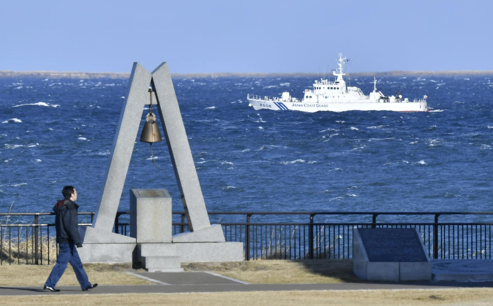 A man walks by the Bell of Hope on Cape Nosappu at the tip of Nemuro Peninsula in Nemuro in Japan's northernmost major island of Hokkaido as a Japan Coast Guard ship patrols in the waters between Hokkaido and an island that belongs to the Habomai Islands, one of four southern Kuril islands, which Japan calls the Northern Territories, seen above the horizon Thursday, Dec. 15, 2016. The leaders of Russia and Japan held talks at a hot springs resort in western Japan on Thursday on a territorial dispute over the Northern Territories that has divided their countries for 70 years. (Yoshiaki Sakamoto/Kyodo News via AP)