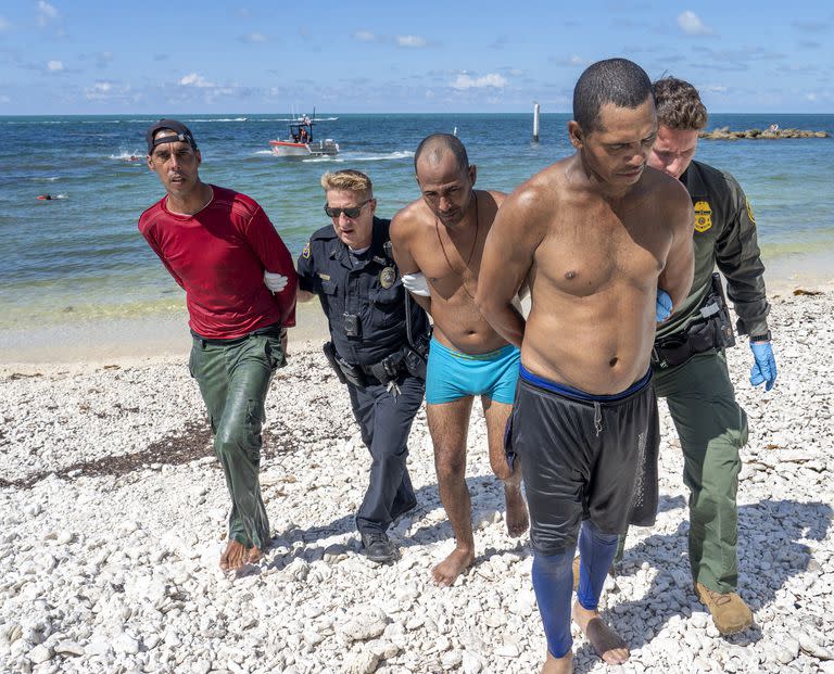 Agentes de la patrulla fronteriza de Estados Unidos se llevan detenidos a 17 migrantes cubanos en Key West, Florida, mientras otros nadan a la playa tras saltar de su bote