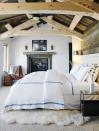 <p>Bright walls, plush bedding, and a fur rug contrast the rough-hewn fireplace mantel and wood vaulted ceiling in this sunny master bedroom by <a href="https://deringhall.com/interior-designers/kathy-kuo-designs" rel="nofollow noopener" target="_blank" data-ylk="slk:Kathy Kuo Designs;elm:context_link;itc:0;sec:content-canvas" class="link ">Kathy Kuo Designs</a>.</p>