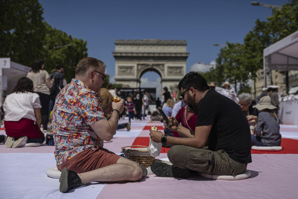 Varias personas comen sus almuerzos como parte de un picnic masivo en los Campos Elíseos, frente al Arco del Triunfo, el domingo 26 de mayo de 2024, en París. (AP Foto/Aurelien Morissard)