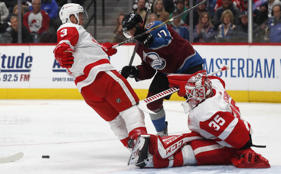 Detroit Red Wings goaltender Jimmy Howard, right, kicks out the puck after stopping a shot off the stick of Colorado Avalanche center Tyson Jost, center, as Red Wings defenseman Alex Biega covers in the first period of an NHL hockey game Monday, Jan. 20, 2020, in Denver. (AP Photo/David Zalubowski)