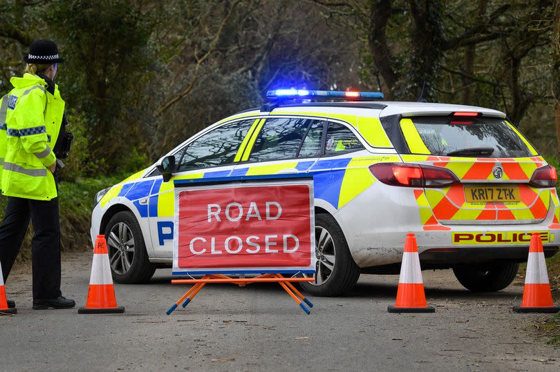 A police car parked in the road behind a 'road closed' sign