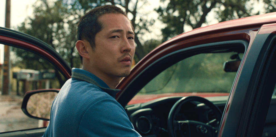 Yeun looks over his shoulder next to his red toyota tacoma pickup truck. (Netflix)