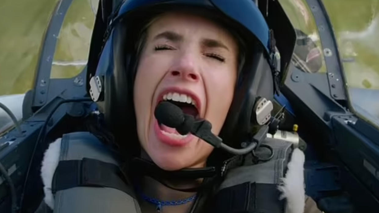  A woman in a fighter pilot helmet screams inside a cockpit. 