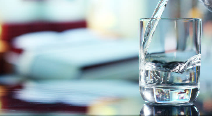 A photo of water being poured into a glass that's sitting on a table.