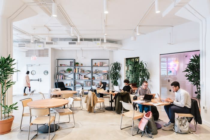 A number of people at various tables in an open workspace.