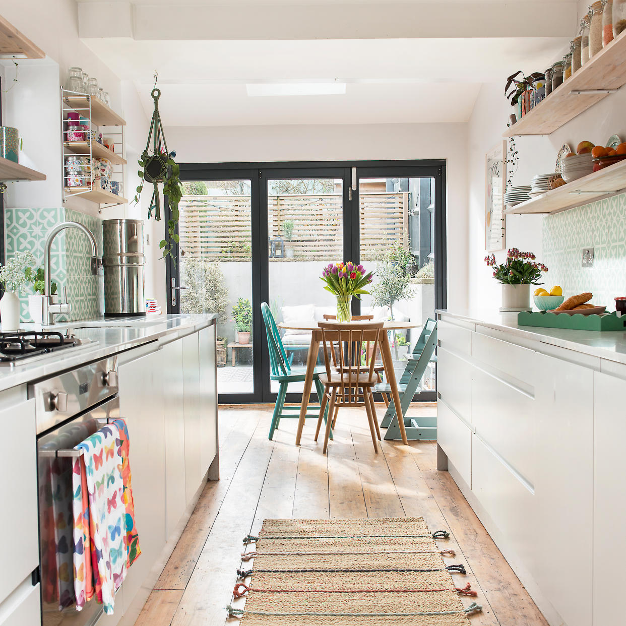  White galley kitchen with open shelving and small wooden dining table 