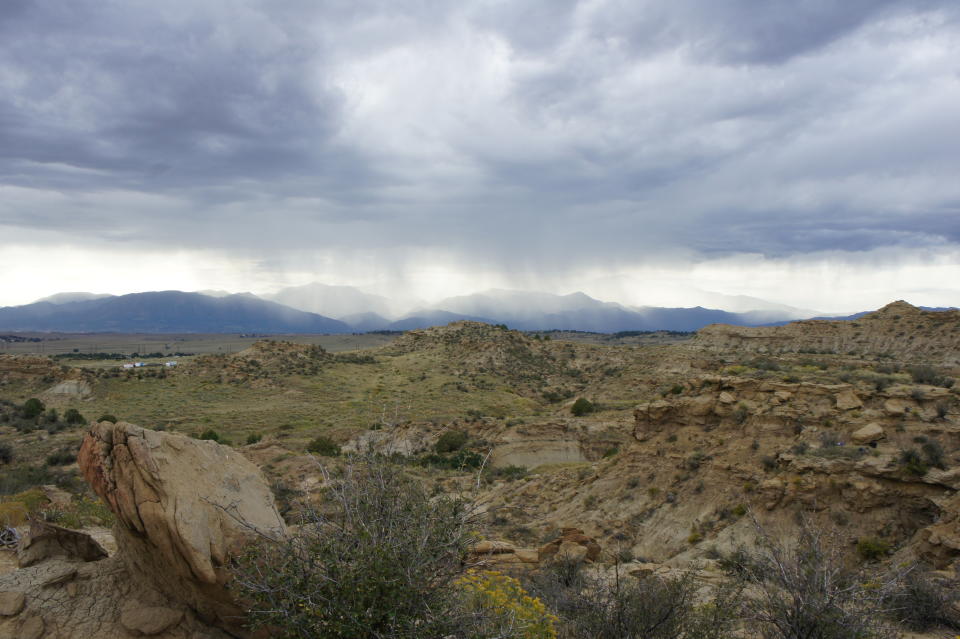 In this photo provided by HHMI Tangled Bank Studios in October 2019, a storm rolls in towards Corral Bluffs, Colo, outside of Denver. The area represents about 300 vertical feet of rock and preserves the extinction of the dinosaurs through the first million years of the Age of the Mammals. The exposure is composed of hard yellow sandstone and mudstones, which represent ancient rivers and floodplains, respectively. (Frank Verock/HHMI Tangled Bank Studios via AP)